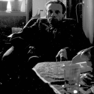 Man sitting indoors, reading newspaper.