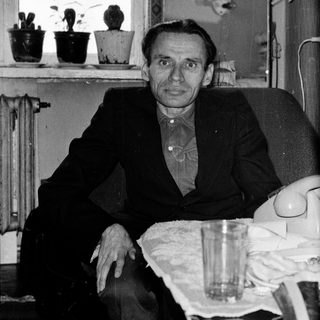 Man sitting indoors near a window with plants.