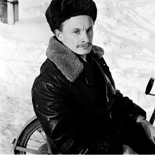 Man in winter attire sitting on bicycle in snowy outdoor setting.