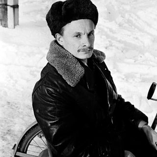 Man in winter attire sitting on bicycle in snowy outdoor setting.