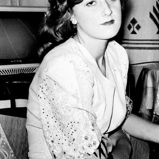 Young woman in vintage clothing, seated indoors.
