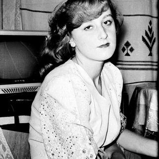 Young woman in vintage clothing, seated indoors.