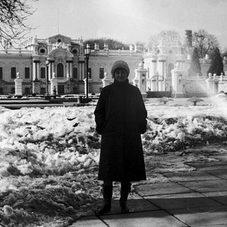 Person standing in snowy park near historic building.