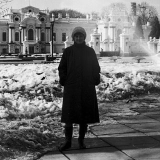 Person standing in snowy park near historic building.