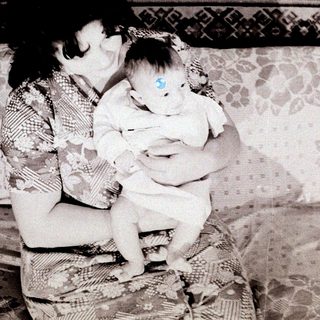 A woman tenderly holds a young baby indoors.