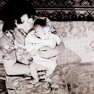 A woman tenderly holds a young baby indoors.