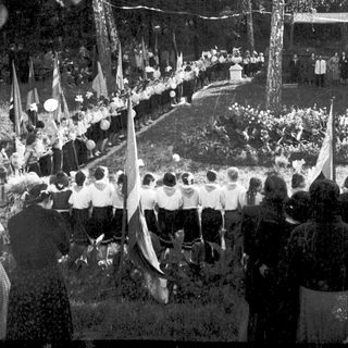 Outdoor gathering with seated attendees, flags, and floral decorations.