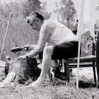 Man shaves dog outdoors near campsite.