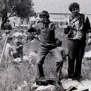 People camping and cleaning in outdoor makeshift settlement.