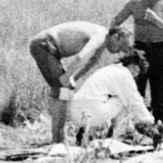 Two men inspecting a fallen soldier in a field.
