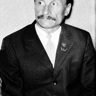 Man in formal attire with mustache and medal pin.
