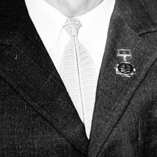 Man in formal attire with mustache and medal pin.