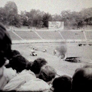 Spectators watch airplane stunt in stadium.