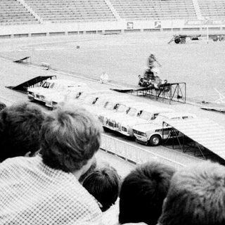 Spectators watch vintage car race on stadium track.