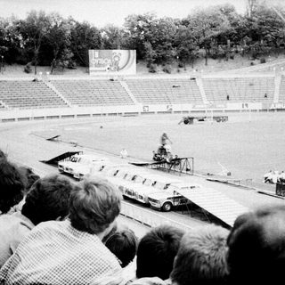 Spectators watch vintage car race on stadium track.