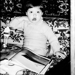 Young child reading book indoors on patterned sofa.