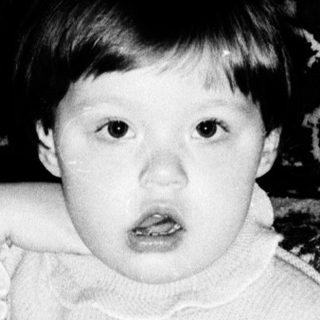 Young child reading book indoors on patterned sofa.