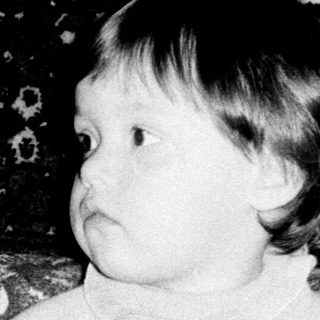 Young child sitting on vintage patterned sofa with toy.