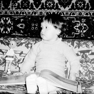Young child sitting on vintage patterned sofa with toy.