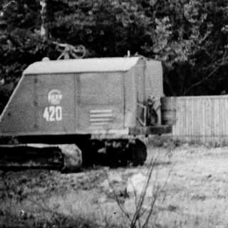 Construction site with bulldozer and cut timber near a fenced building.