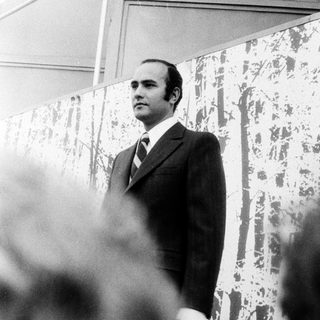 Man in suit speaking at an outdoor event.