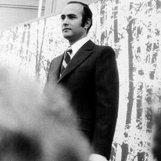 Man in suit speaking at an outdoor event.