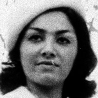 Woman in 1970s-style coat and hat indoors.