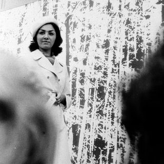 Woman in 1970s-style coat and hat indoors.