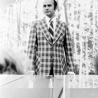 Man in plaid suit, standing indoors.