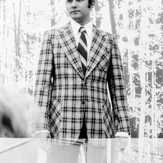 Man in plaid suit, standing indoors.