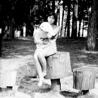 Woman sitting on stumps holding a dog outdoors.