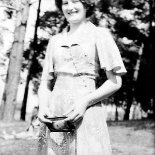 Young woman in vintage nurse's uniform smiling outdoors.