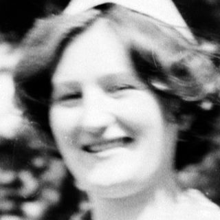 Young woman in vintage nurse's uniform smiling outdoors.