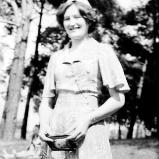 Young woman in vintage nurse's uniform smiling outdoors.