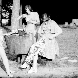 Four people outdoors by a barrel, likely washing clothes.