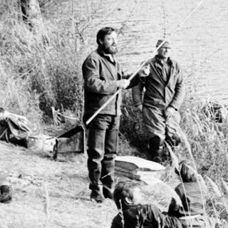 Two men fishing by a lake shore.