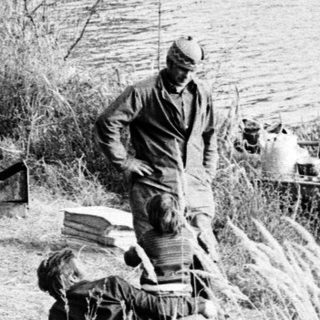 Three men by a frozen lake preparing boat.