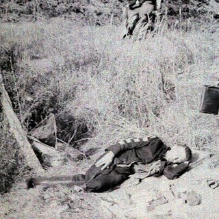 Child carrying bucket near fallen soldier in wartime terrain.