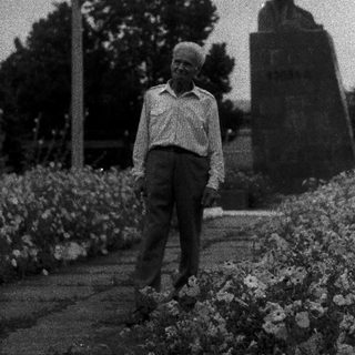 Man standing beside a bust statue in a park.