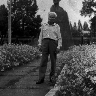 Elderly man standing beside a statue in park.