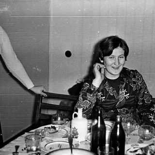 Woman smiling at table during indoor gathering.