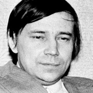 Man in 1970s-style suit seated indoors.
