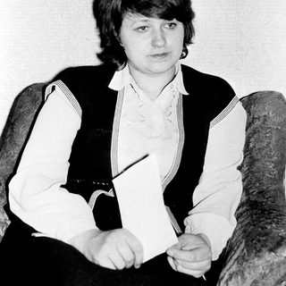 Woman sitting in armchair holding pencil.