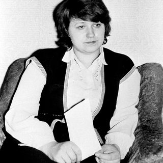 Woman sitting in armchair holding pencil.