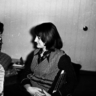 Two women at a table, one resting head, other smiling.