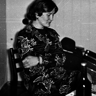 Woman seated at table with microphone, possibly speaking.
