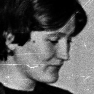 Woman seated at table with microphone, possibly speaking.