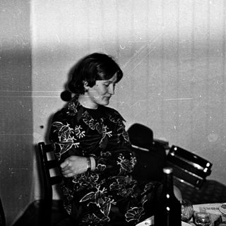 Woman seated at table with microphone, possibly speaking.