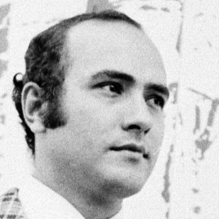 Man in plaid suit standing indoors near abstract artwork.