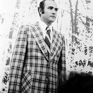 Man in plaid suit standing indoors near abstract artwork.